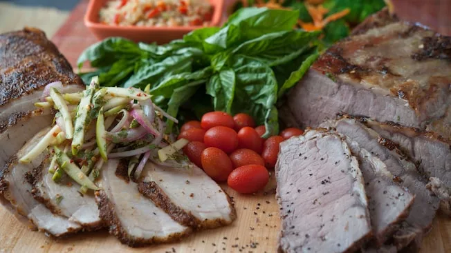 Slices of pork and steak with grape tomatoes and basil on cutting board